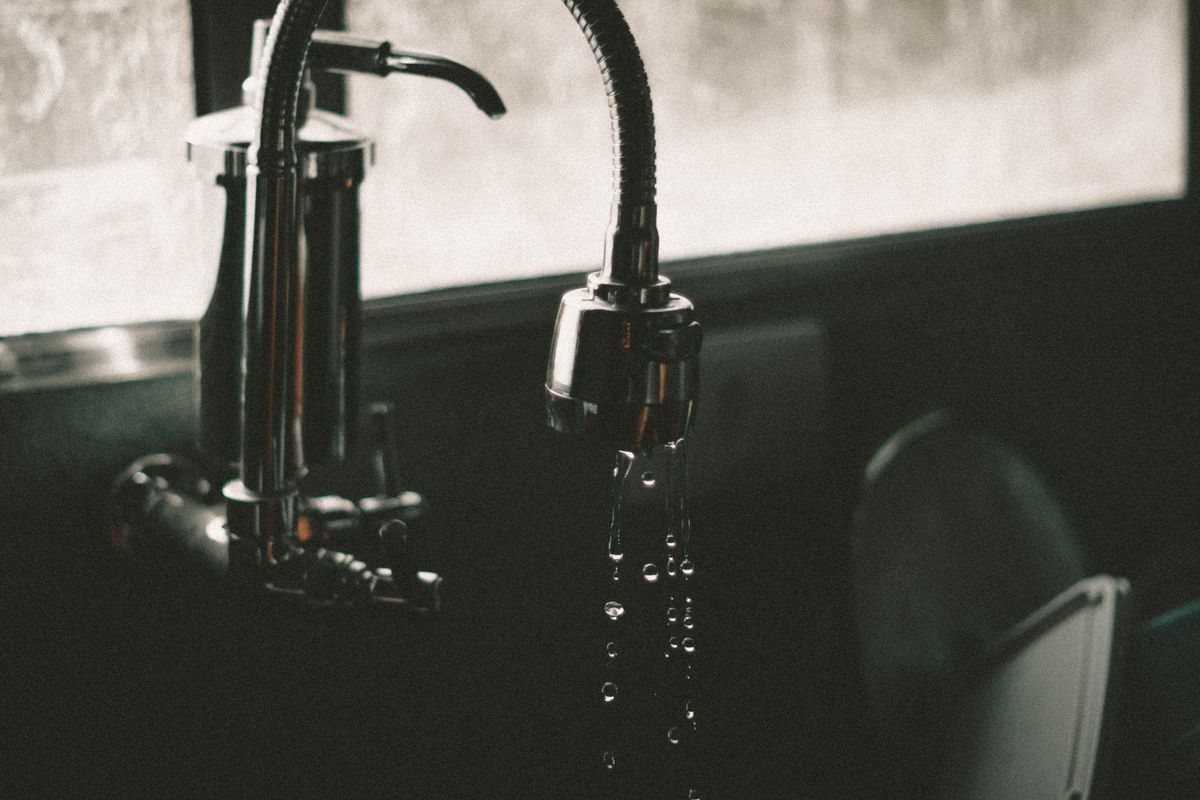 Dark kitchen faucet with water droplets falling into a sink.